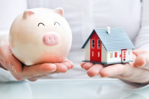 Hands holding a piggy bank and a house model. Save money when moving.