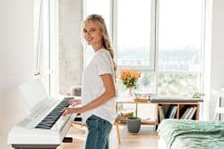 Side view of young woman playing electronic piano moved to side of room