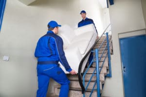 Male movers carrying sofa while climbing steps at home