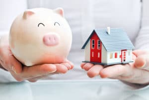 Hands holding a piggy bank and a house model. Save money when moving. Reduce your Moving Costs