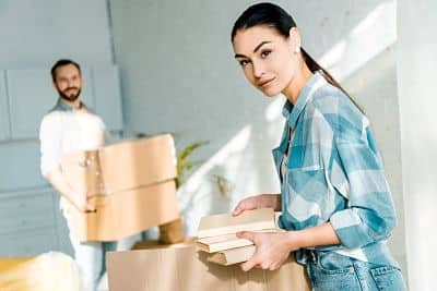 Beautiful wife putting books in cardboard box while husband holding cardboard boxes, moving concept