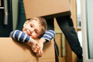 Professional Movers carrying moving boxes and a child safely out of the way inside a moving box.