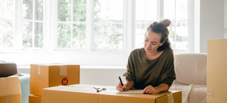 A woman writing on a box and waiting movers Milford CT offers