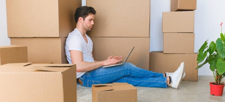 A man using his laptop and sitting among boxes waiting for movers Trumbull CT