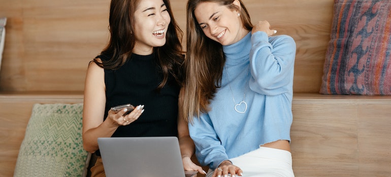 Two women using a laptop and a phone