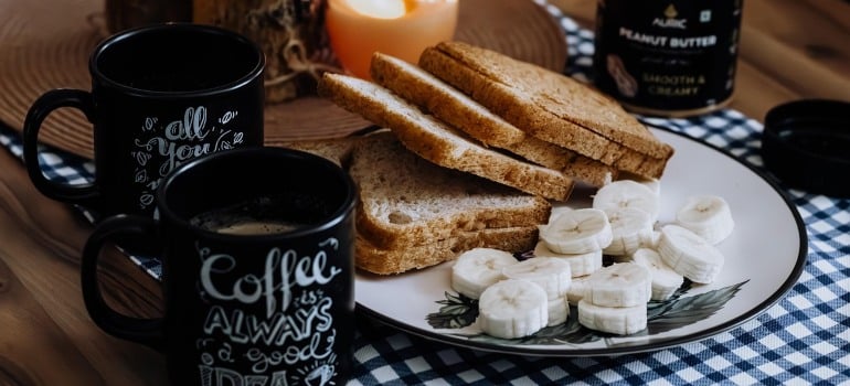 A plate with sliced bananas and toast, and next to it, some candles and two cups of coffee.