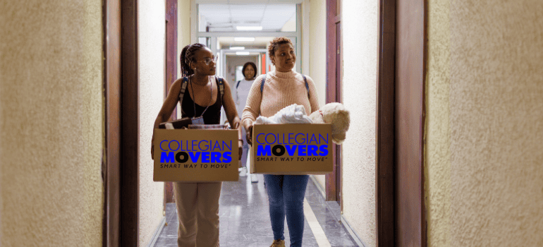 mother and daughter during the college move in process walking down the hall with boxes 