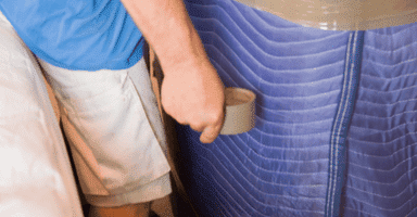 Mover carefully blanket wrapping furniture for protection.